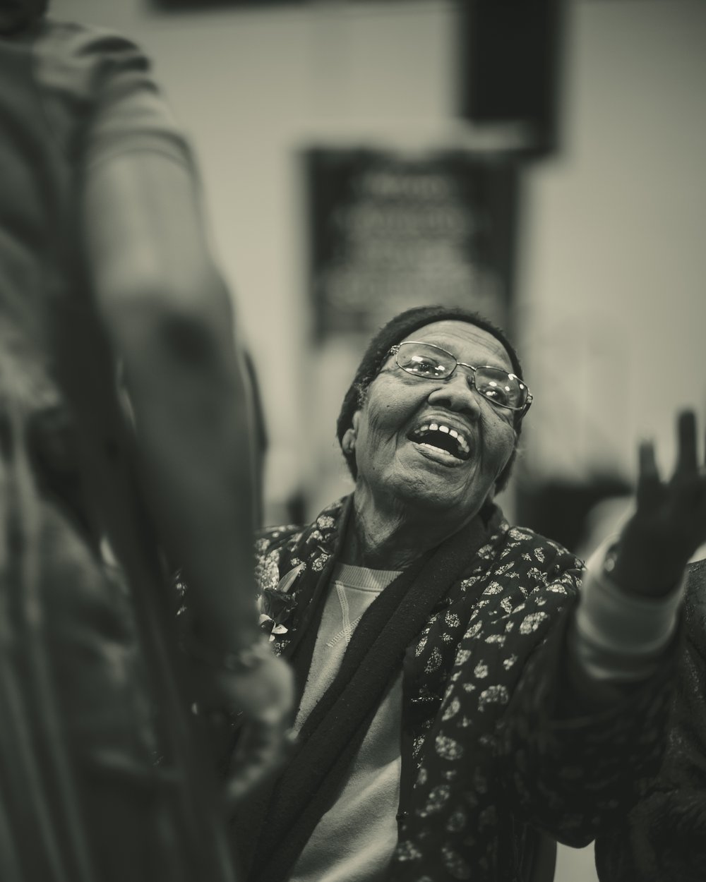 A Black Creole elder woman laughing with her arms open at a community gathering