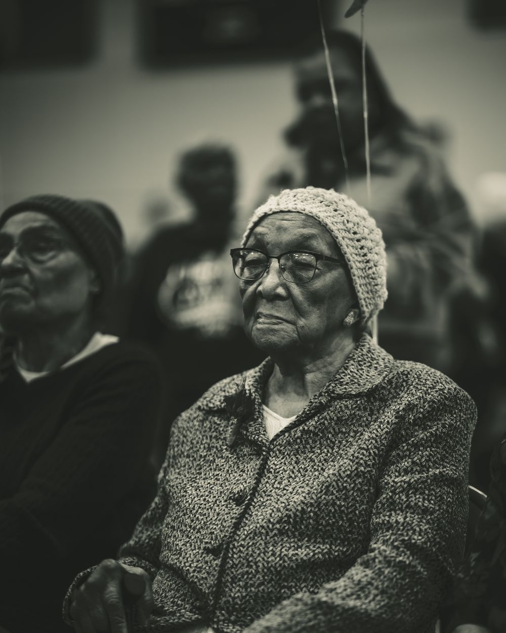Two Black Creole elders seated together, one in a knit cap, at a community gathering